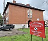 Red New Philadelphia City Schools administrative office sign in front of a brick building and parked vehicle.