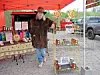 A vendor stands behind a table of products under a red tent at an outdoor market.