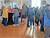 People standing and conversing in a bright indoor room with hardwood floors.