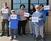 Several people standing outside a building holding signs with logos and text.