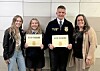 Four people stand indoors holding certificates and posing for a photo.