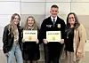 Four people stand indoors holding certificates and posing for a photo.