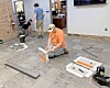 Workers installing flooring inside a commercial room with tools and material samples on the floor.