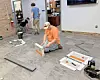 Workers installing flooring inside a commercial room with tools and material samples on the floor.