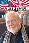 Smiling older man in a scarf with an American flag graphic and the word “VETERAN” above him.