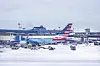 American Airlines jet parked on a snowy airport apron near terminal buildings and ground vehicles.