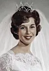Portrait of a smiling woman wearing a crown and a white lace dress.
