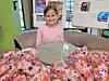 A smiling child sits at a table with a red, white and blue star-patterned costume displayed in front of her.