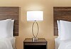 Hotel room with two beds, wooden headboards, and a bedside lamp centered between them.
