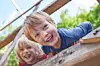 Two smiling children lean over a wooden playground structure outdoors.