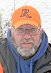 Man in glasses and an orange cap with an R logo outdoors near water.