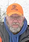 Man in glasses and an orange cap with an R logo outdoors near water.
