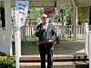 Man in sunglasses speaks at a podium outdoors under a pavilion.