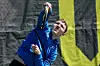 Man in a blue jacket celebrating with raised arms in front of a black-and-yellow backdrop.