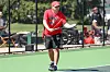 A man in red holds a tennis racket on an outdoor court with people seated behind a fence.