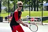 Tennis player in sunglasses swings a racket on an outdoor court.