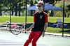 Tennis player in red and black clothing holding a racket on an outdoor court.