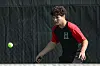 Tennis player in black and red shirt watches a green ball in front of a dark backdrop.