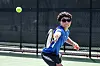 Tennis player in blue shirt reaching toward a ball on an outdoor court.