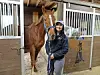 Woman holding a horse’s lead rope in a stable beside a brown horse with a white blaze.