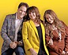 Three people seated closely together and smiling against a yellow background.