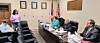 Officials seated around a conference table in a meeting room with flags and framed certificates.