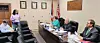 Officials seated around a conference table in a meeting room with flags and framed certificates.