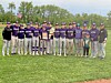 A youth baseball team stands in a line on a grassy field, holding trophies and banners.