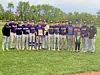 A youth baseball team stands in a line on a grassy field, holding trophies and banners.