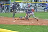 Baseball player sliding into home plate while catcher tags him out in front of the dugout and stands.