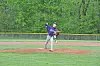 A baseball pitcher in a purple jersey throws a pitch on a grassy field.