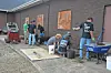 Workers stand beside a brick building, fitting and finishing large wall panels on a concrete walkway.