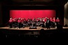 Large band performing on stage under red lighting in a concert hall.