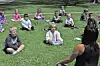 Children sitting on grass in a park, with an adult facing them in the foreground.