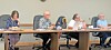 Several people seated at a long table in a meeting room with laptops and papers.