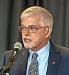Man in glasses speaking into a microphone indoors.