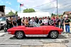 A red classic sports car parked outdoors with a crowd standing behind it.