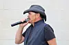 Man in a dark cowboy hat speaking into a handheld microphone.