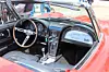 Interior of a red classic convertible with a wood-rim steering wheel, dashboard gauges and manual gear shift.
