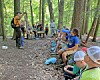 A group seated and standing on a forest trail while an instructor speaks at left.