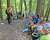 A group seated and standing on a forest trail while an instructor speaks at left.