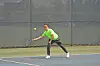 Tennis player in green shirt reaching to hit a ball on an outdoor court.