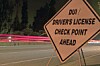 Roadside sign warning of a driver's license checkpoint ahead beside a blurred road at night.