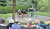 Audience seated outdoors watching two musicians perform on a small circular stage in a park.