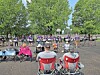 People seated in folding chairs and standing on a basketball court in a park with trees in the background.