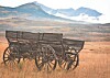 Old wooden wagon standing in a grassy field with mountains behind it.