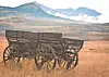 Old wooden wagon standing in a grassy field with mountains behind it.