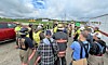 Workers wearing hard hats and safety vests gather at a construction site near vehicles and portable structures.
