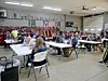 People seated at folding tables in a fire station training room with trophies and equipment along the wall.