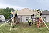 Construction workers build a wooden roof frame on a small building outdoors.
